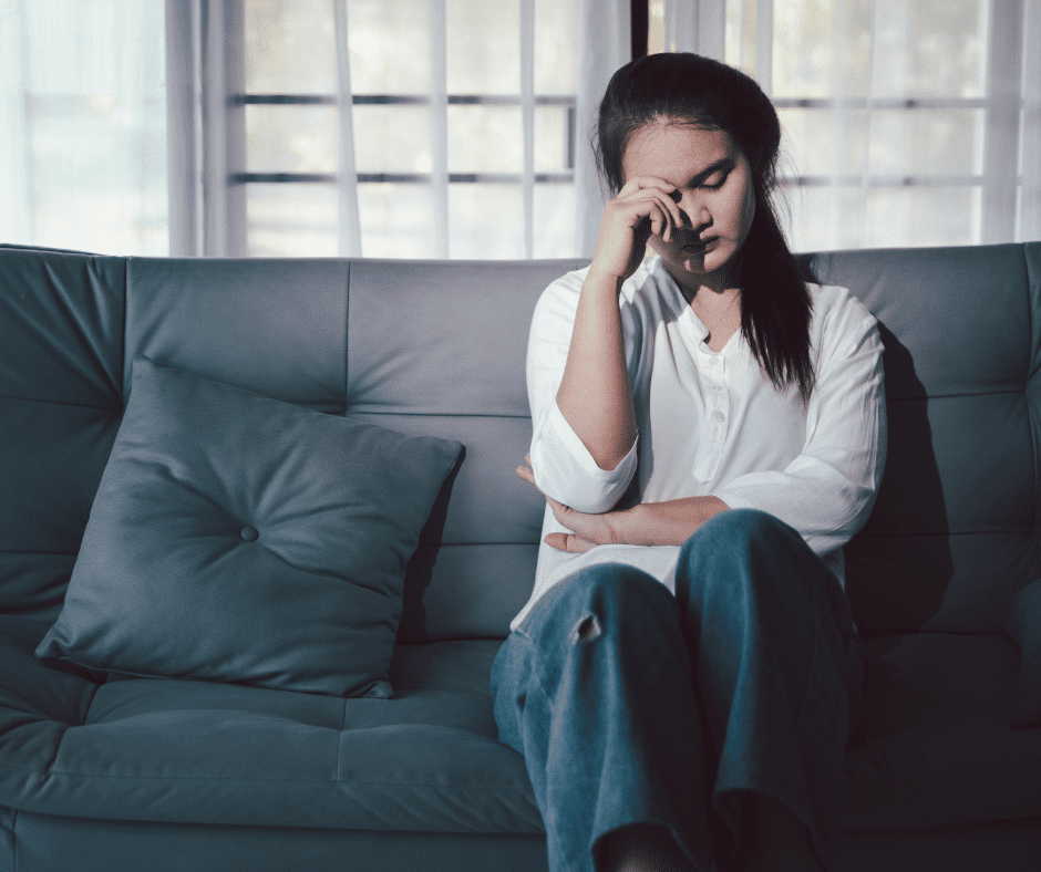 tired caregiver sits on the couch in jeans and white shirt